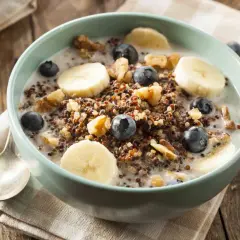 Miseczka pełna owsianki proteinowej z bananem, borówkami i orzechami na drewnianym stole.