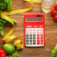 Czerwony kalkulator obok miarki i świeżych warzyw. Zastanawiasz się, ile to kcal? Oblicz swoją dietę!