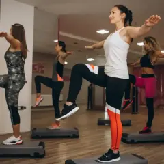 Kobiety wykonują trening aerobowy na stepach, podnosząc kolana i wyciągając ręce.