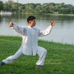 Mężczyzna w białym stroju ćwiczy tai chi co to za sztuka walki, harmonijnie poruszając się nad jeziorem.