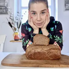 Kobieta zastanawia się, jaki chleb na odchudzanie wybrać. Na desce leżą dwa bochenki ciemnego pieczywa.