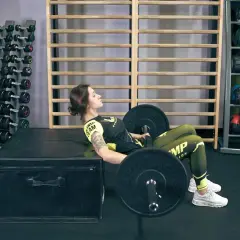 Kobieta wykonuje ćwiczenie hip thrusts z obciążeniem na ławce w siłowni.