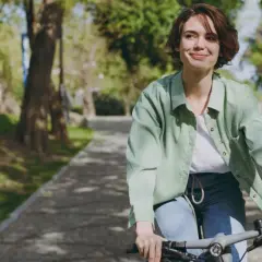 Uśmiechnięta kobieta na rowerze w parku. Aktywność fizyczna to klucz do tego, jak podkręcić metabolizm po 40.