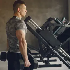 Mężczyzna z hantlami, ćwiczący triceps w siłowni.