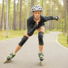 Kobieta w kasku i ochraniaczach jeździ na rolkach po leśnej ścieżce, spalając kalorie.