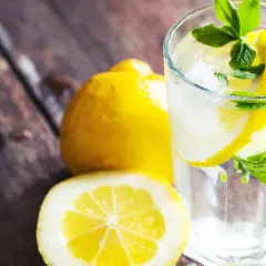 Orzeźwiająca woda z cytryną i miętą, z cytrynami w tle. Picie wody z cytryną daje energię i wspiera trawienie.