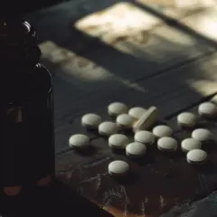 Butelka z lekami i garść tabletek, wśród nich jedna podłużna. Może to suplement z treoniną?