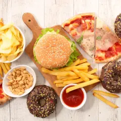Uczta z niezdrowym jedzeniem: burgery, frytki, pizza, pączki, chipsy i orzeszki.