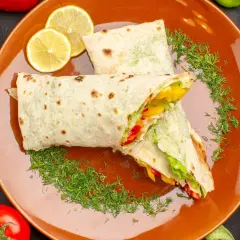 Dwa pyszne wrapy z warzywami i kurczakiem, podane na pomarańczowym talerzu z plasterkami cytryny i koperkiem. Idealny fit tortilla na szybki posiłek.