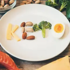 Czy dieta keto jest zdrowa? Na talerzu litery KETO z sera, orzechów, brokuła i jajka. Wokół łosoś, awokado, oliwa.