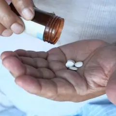 Dłoń z kilkoma tabletkami, które wypadły z brązowej buteleczki. Pytanie brzmi: kiedy brać potas?