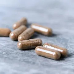 Kilka kapsułek ashwagandhy na szarym tle. Dyskusje o ashwagandha skutki uboczne forum często poruszają temat bezpieczeństwa suplementów.