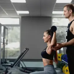 Trener personalny pomaga kobiecie w ćwiczeniu tricepsów. Pokazuje, jakie partie mięśni ćwiczyć razem dla efektywnego treningu.