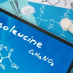 Na ekranie tabletu widnieje nazwa "Isoleucine" oraz wzór chemiczny. Obok leżą próbki białego proszku, przypominające izoleucynę.