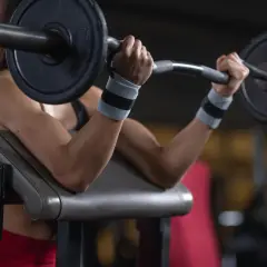 Kobieta ćwiczy biceps na modlitewniku, podnosząc sztangę. Zastanawiasz się, ile waży gryf?