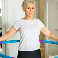Kobieta w białej koszulce ćwiczy z hula hop w domu.