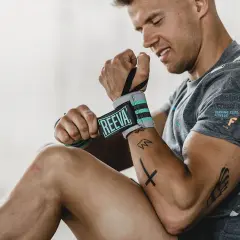 Mężczyzna przygotowuje się do ćwiczeń na nadgarstek, zakładając opaski z logo REEVA.