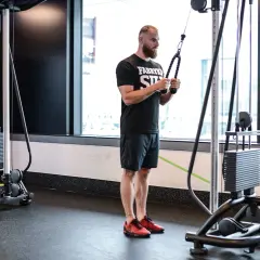 Mężczyzna wykonuje ćwiczenie na triceps, znane jako skull crushers, używając wyciągu.