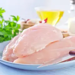 Surowe piersi z kurczaka na talerzu, obok pęczek natki, oliwa i przyprawy. Dowiedz się, ile białka ma pierś z kurczaka.