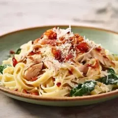 Pyszny makaron ze szpinakiem i kurczakiem w sosie śmietanowym, posypany parmezanem i chrupiącym boczkiem.