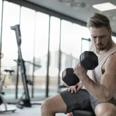 Mężczyzna ćwiczy biceps z hantlem, doskonaląc swoją biomechanikę. W tle siłownia z maszynami.