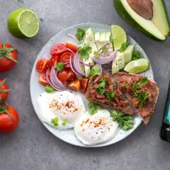 Śniadanie idealne na dietę 1500 kcal: jajka w koszulce, tost z pastą, awokado, pomidorki, cebula i limonka.