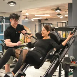 Trener pomaga kobiecie na maszynie do przysiadów. Jej nogi wykonują ruchy, jakby spinning, podczas ćwiczeń.
