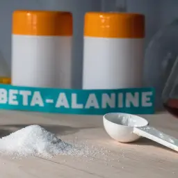 Biały proszek, miarka i etykieta z napisem BETA-ALANINE na tle laboratoryjnego sprzętu.