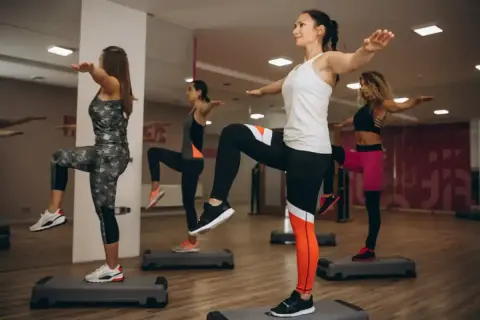 Kobiety wykonują trening aerobowy na stepach, podnosząc kolana i wyciągając ręce.