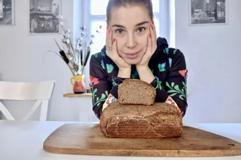 Kobieta zastanawia się, jaki chleb na odchudzanie wybrać. Na desce leżą dwa bochenki ciemnego pieczywa.