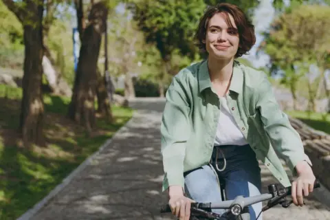 Uśmiechnięta kobieta na rowerze w parku. Aktywność fizyczna to klucz do tego, jak podkręcić metabolizm po 40.