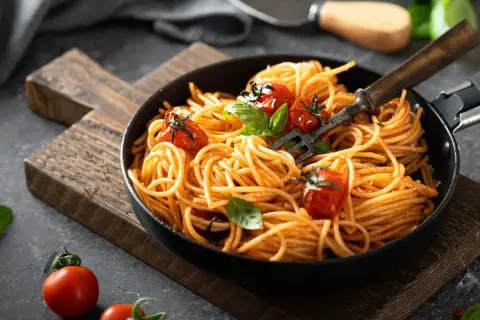 Pyszne danie z makaronem spaghetti w sosie pomidorowym, udekorowane świeżymi pomidorkami i bazylią. Idealne na szybki obiad.