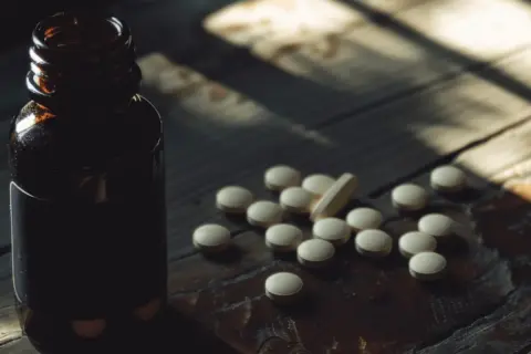 Butelka z lekami i garść tabletek, wśród nich jedna podłużna. Może to suplement z treoniną?