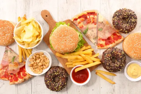 Uczta z niezdrowym jedzeniem: burgery, frytki, pizza, pączki, chipsy i orzeszki.