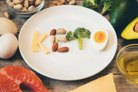 Czy dieta keto jest zdrowa? Na talerzu litery KETO z sera, orzechów, brokuła i jajka. Wokół łosoś, awokado, oliwa.