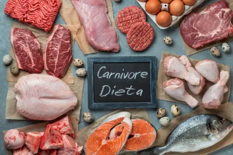 Różnorodne mięsa i ryby, jajka, kości. Tabliczka z napisem "Carnivore Dieta" sugeruje menu dla miłośników mięsa.