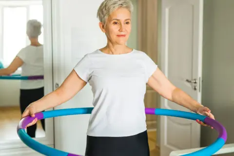 Kobieta w białej koszulce ćwiczy z hula hop w domu.