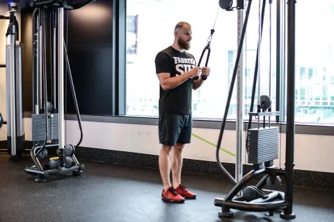 Mężczyzna wykonuje ćwiczenie na triceps, znane jako skull crushers, używając wyciągu.