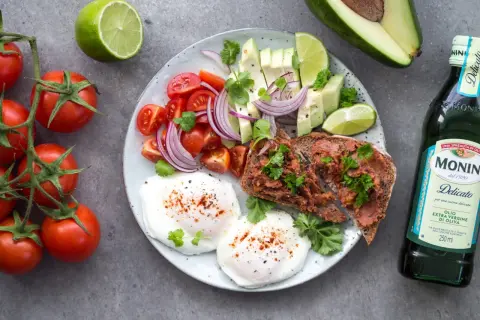 Śniadanie idealne na dietę 1500 kcal: jajka w koszulce, tost z pastą, awokado, pomidorki, cebula i limonka.