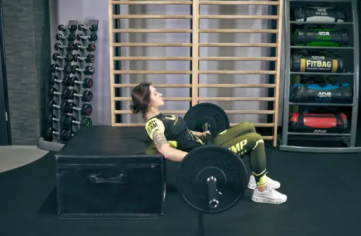 Kobieta wykonuje ćwiczenie hip thrusts z obciążeniem na ławce w siłowni.