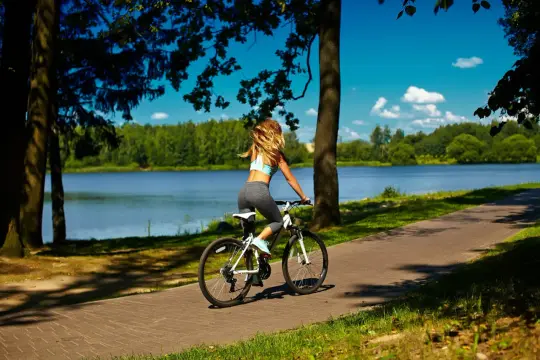 Kobieta na rowerze cieszy się pięknymi trasami rowerowymi na Mazurach, nad jeziorem.