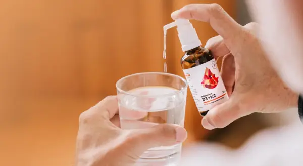 Dłoń dozuje witaminę D3+K2 do szklanki wody. To najlepsza witamina D3, jaką można wybrać dla zdrowia.