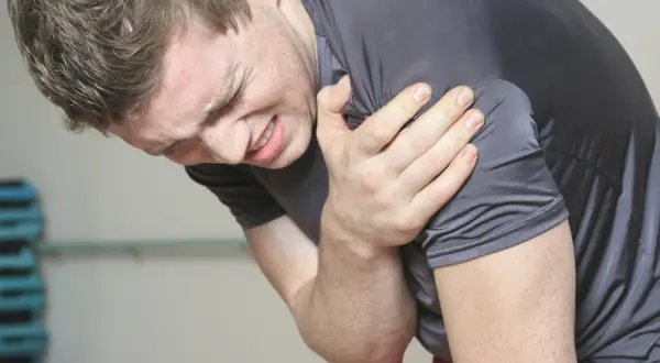Mężczyzna z bólem trzyma się za ramię, cierpiąc z powodu naderwanego bicepsa po treningu.