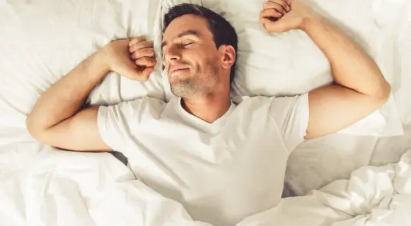 Uśmiechnięty mężczyzna rozciąga się w łóżku. Nawet podczas snu organizm spala kalorie bez wysiłku.