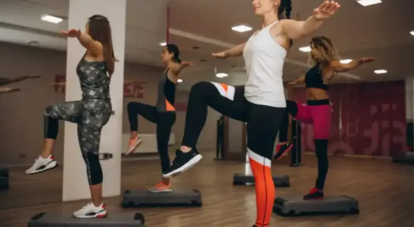 Kobiety wykonują trening aerobowy na stepach, podnosząc kolana i wyciągając ręce.