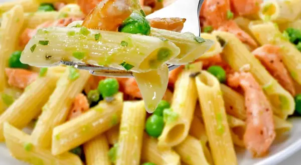 Penne z łososiem i groszkiem, polane kremowym sosem. Widok z bliska na widelcu.