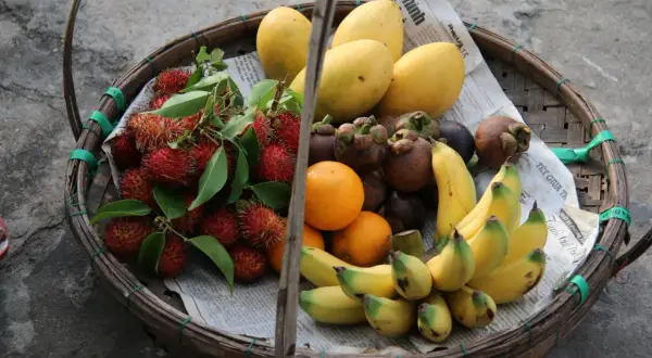 Koszyk pełen owoców: liczi, mango, pomarańcze, mangostany i banany. To idealne, lekkostrawne owoce na zdrową przekąskę.