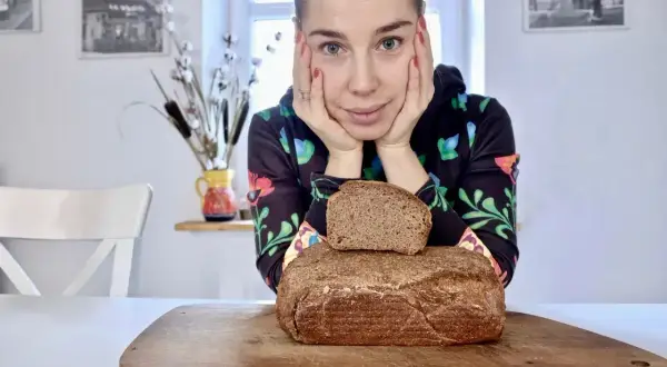 Kobieta zastanawia się, jaki chleb na odchudzanie wybrać. Na desce leżą dwa bochenki ciemnego pieczywa.