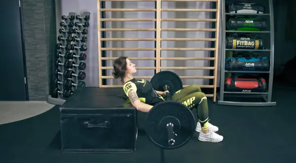 Kobieta wykonuje ćwiczenie hip thrusts z obciążeniem na ławce w siłowni.