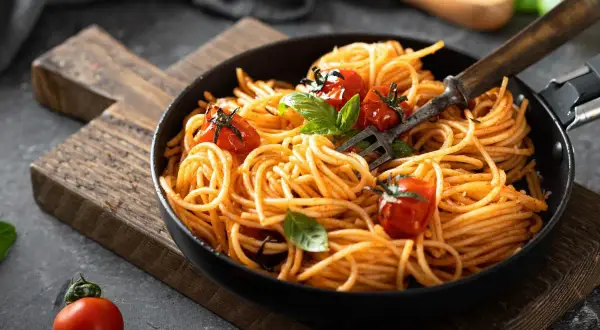 Pyszne danie z makaronem spaghetti w sosie pomidorowym, udekorowane świeżymi pomidorkami i bazylią. Idealne na szybki obiad.